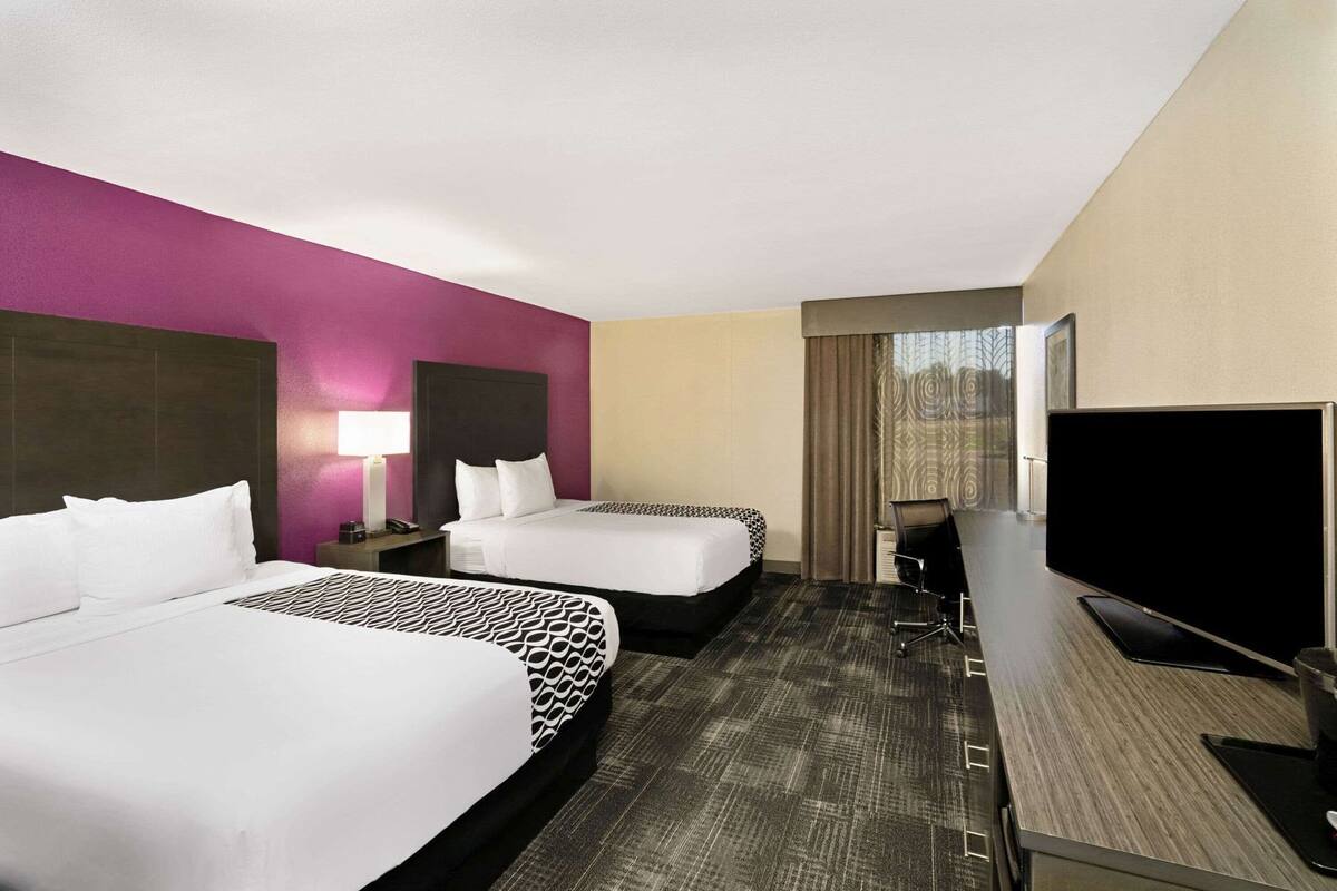 A hotel room with two beds, a desk, a TV, and a window with curtains.