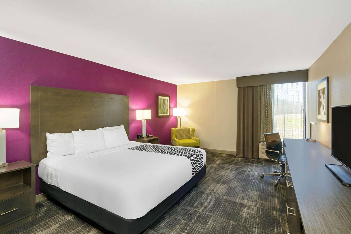 A hotel room with a large bed, a desk, a chair, and a TV.
