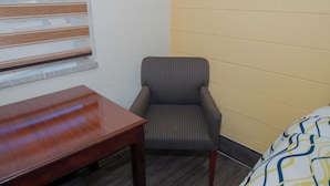 A corner room with a wooden table, a patterned armchair, and a bed with a patterned bedspread. - South Wind Inn (Liberal)