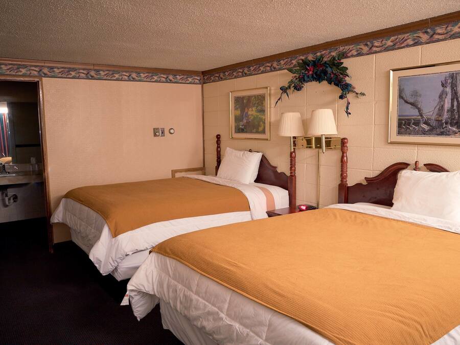 Habitación de hotel con dos camas, cabecero de madera, un espejo, un escritorio con lámpara y un cuadro en la pared.