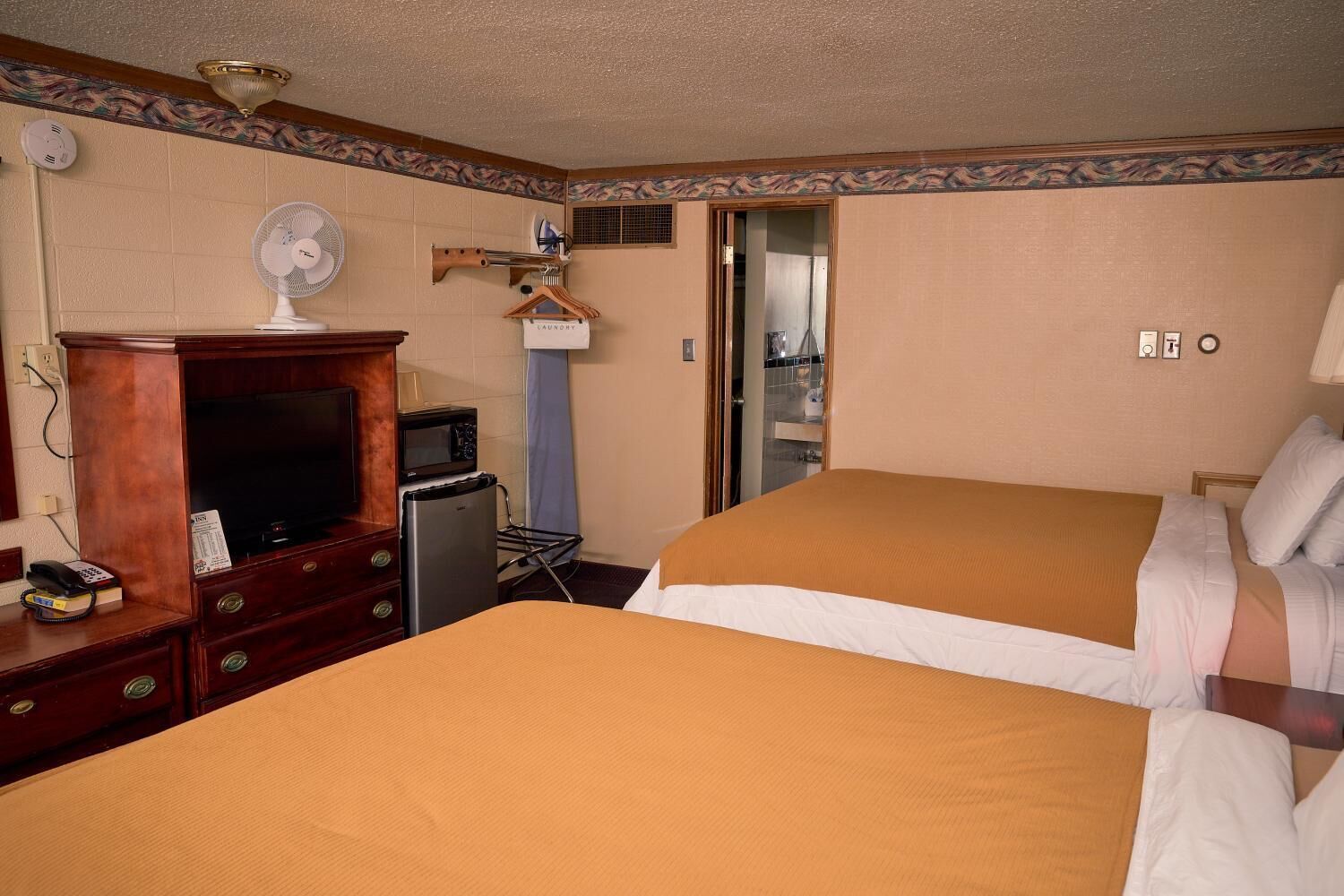 Quarto de hotel com duas camas, cómoda de madeira, micro-ondas, ventoinha e pequeno frigorífico.