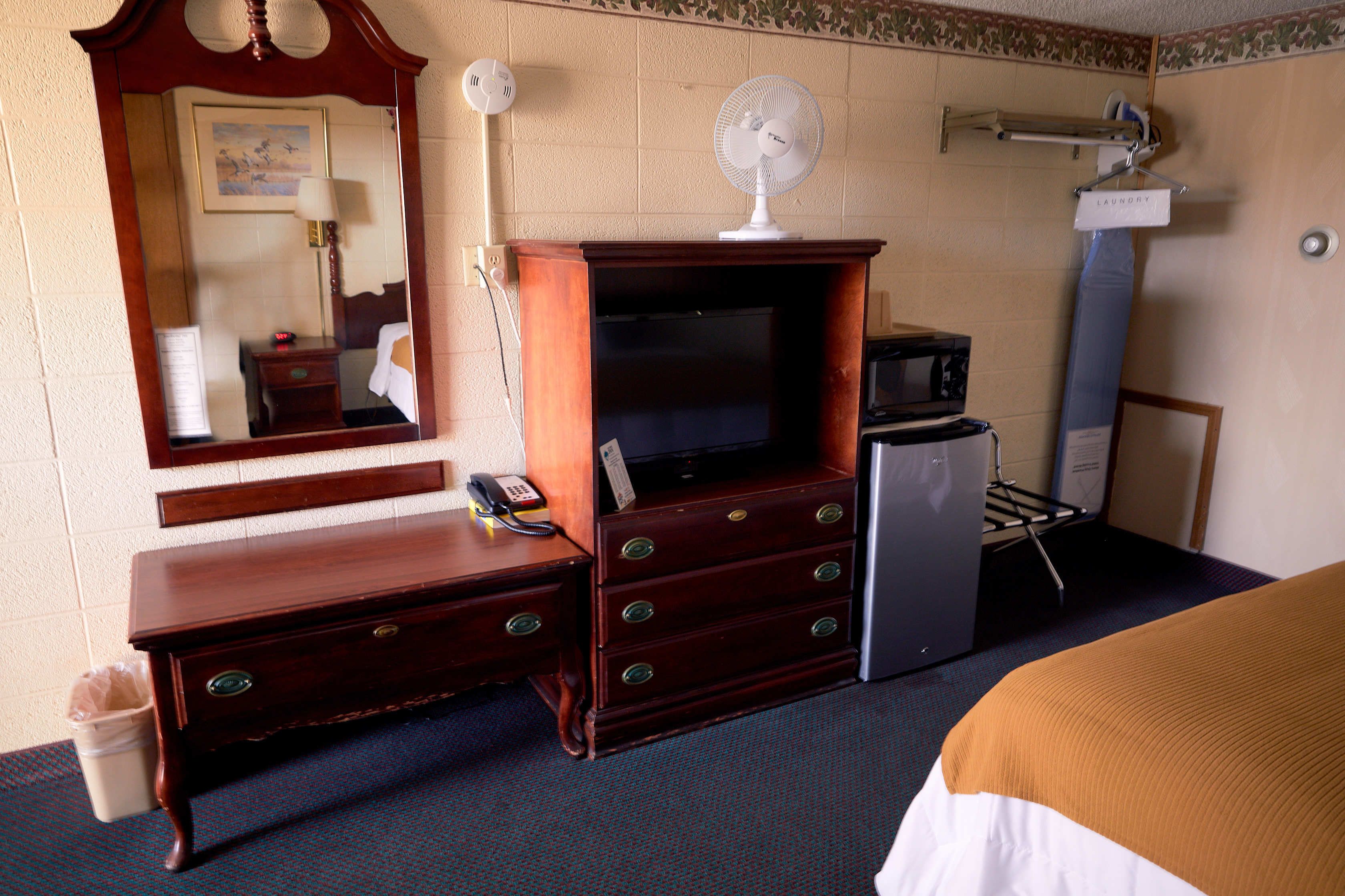 A hotel room with a wooden dresser, a television, a microwave, and a bed with a brown and white bedspread.