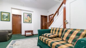 Een woonkamer met een groene bank, een bruine leren fauteuil, een houten bijzettafeltje en twee ingekaderde schilderijen aan de muur.