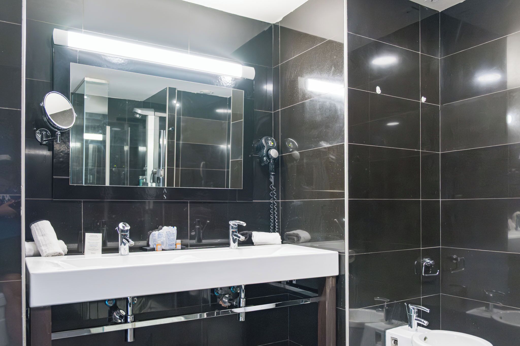 Une salle de bain moderne avec un grand miroir, un lavabo blanc et un sèche-cheveux.