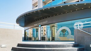 Un edificio moderno con una entrada curva, puertas de vidrio y un letrero que dice 'Bakour La Mango Splash'.