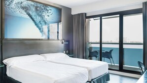 Una habitación de hotel con una cama grande, un escritorio y vistas a la ciudad desde el balcón.
