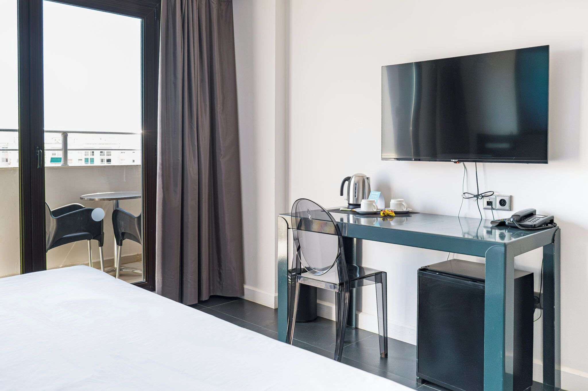 A hotel room with a bed, a desk with a chair, a television, a coffee maker, and a small trash bin.