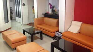 Un vestíbulo de hotel con sofás naranjas, una mesa de centro de vidrio y una pared decorativa roja.