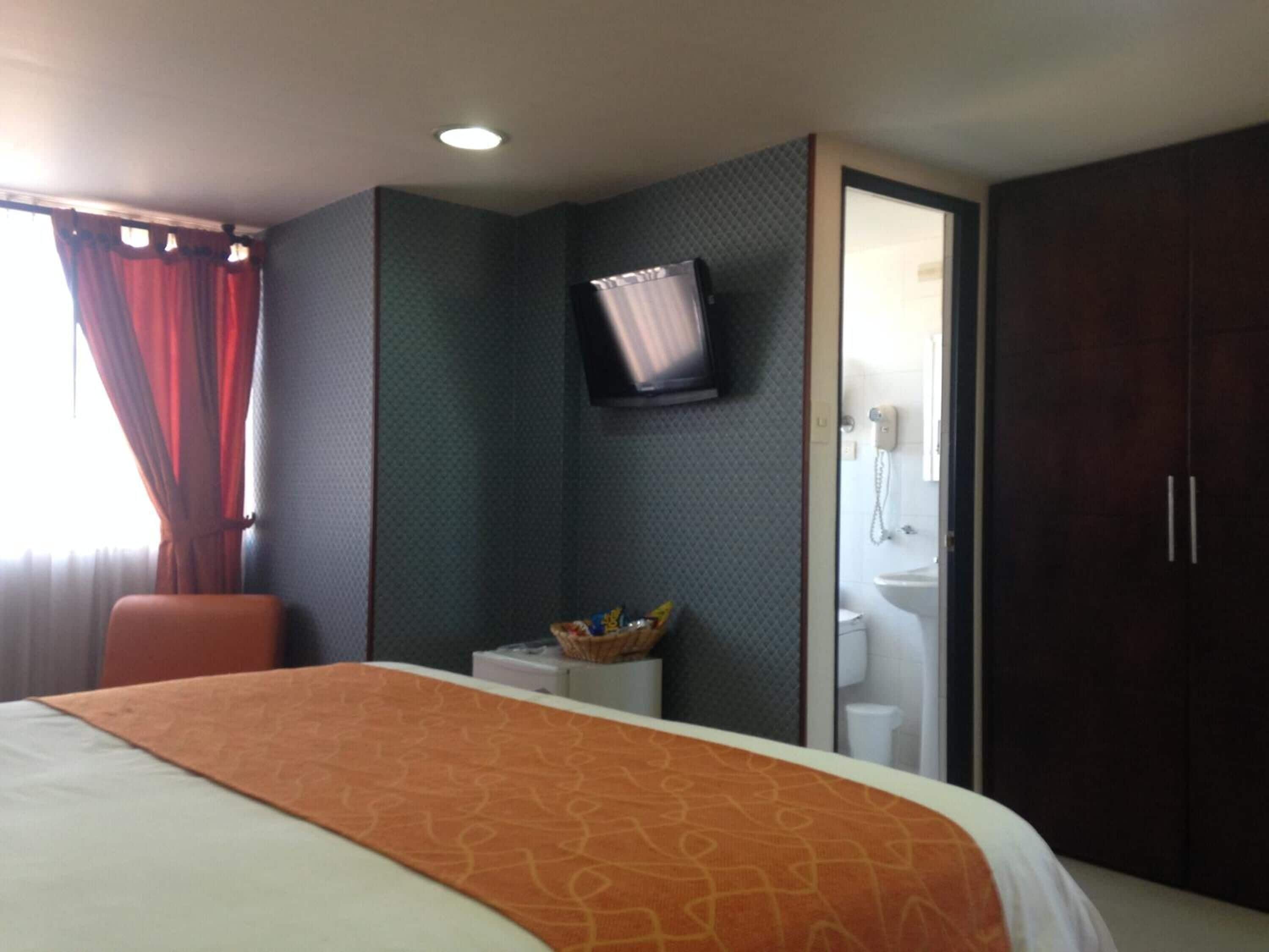 Una camera d'albergo con un letto, una televisione a parete, un piccolo tavolo con un cesto e un armadio.