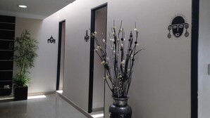 Un pasillo moderno con piso pulido, una planta en maceta y decoración en la pared, incluyendo un jarrón con ramas y un rostro estilizado.