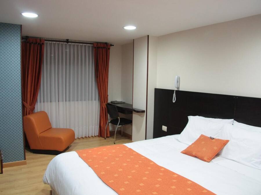 A hotel room with a bed, an orange chair, a desk, and a telephone.