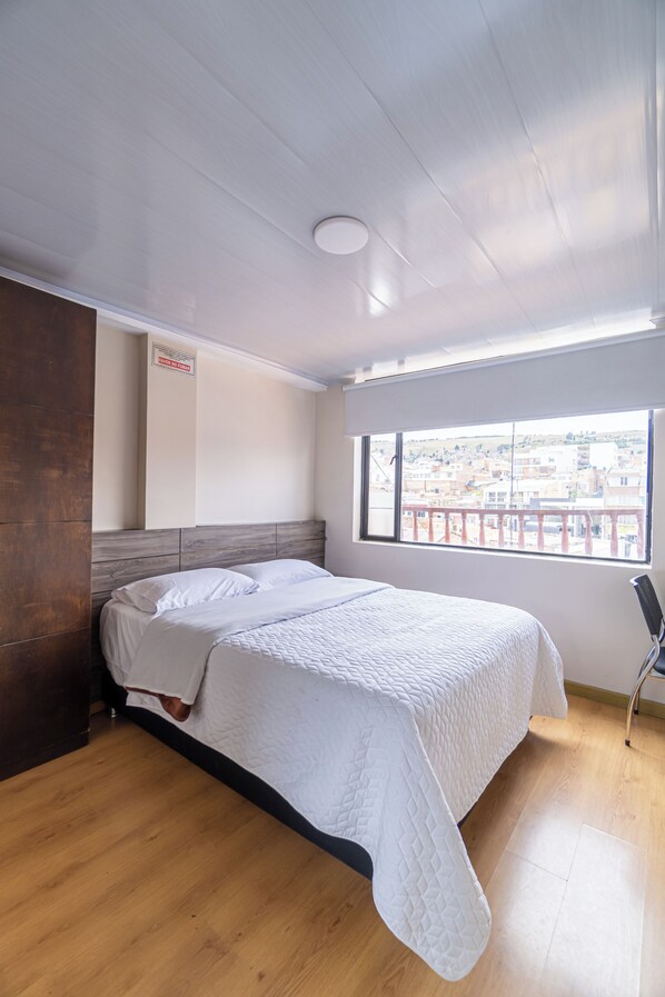 A bedroom with a bed, wooden floor, a window with a view, and a ceiling light.