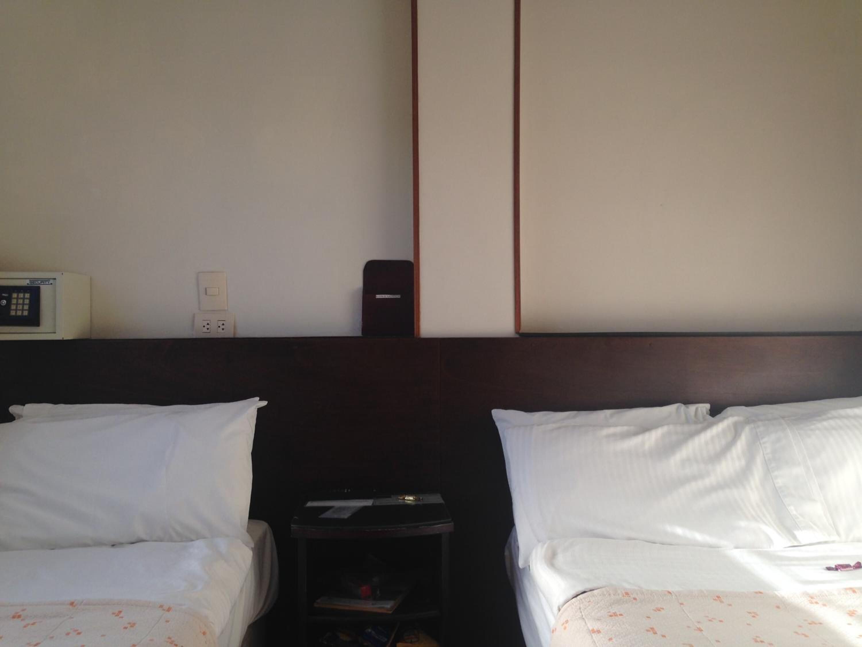 A hotel room with two beds, a bedside table, a small cabinet, and a wall-mounted telephone.