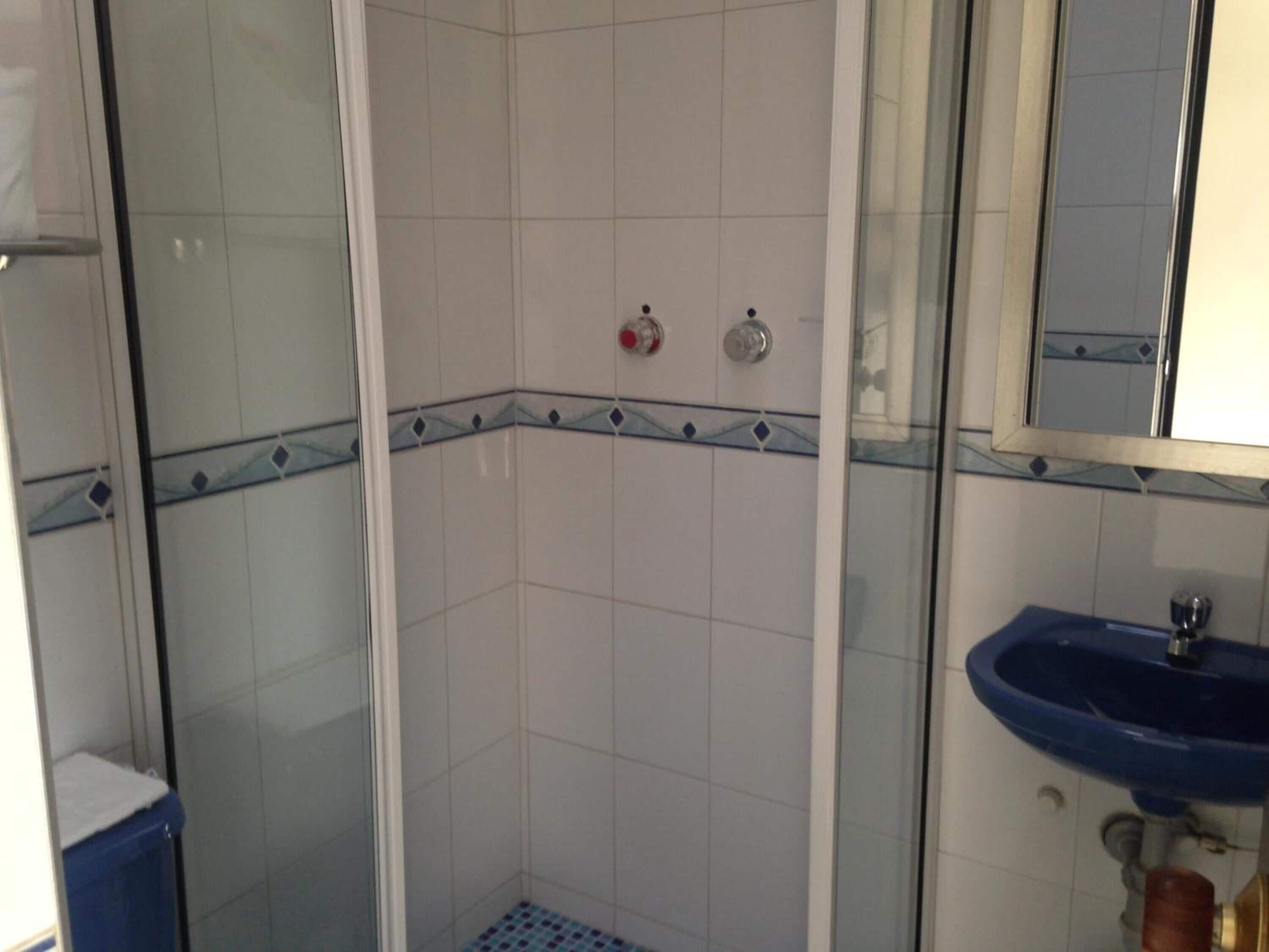 A bathroom with a glass shower enclosure, a blue sink, and a tiled wall with a decorative border.