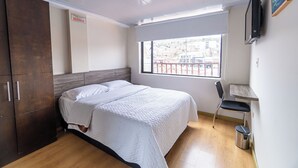 Un dormitorio con cama, armario de madera, escritorio, silla y ventana con vistas.