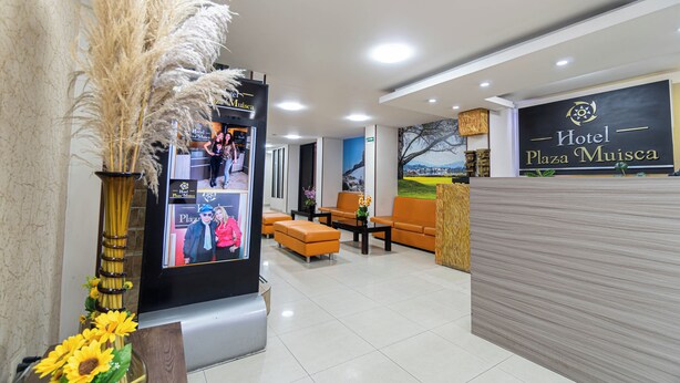 Vestíbulo de hotel con mostrador de recepción, zona de estar y una pantalla grande que muestra imágenes.