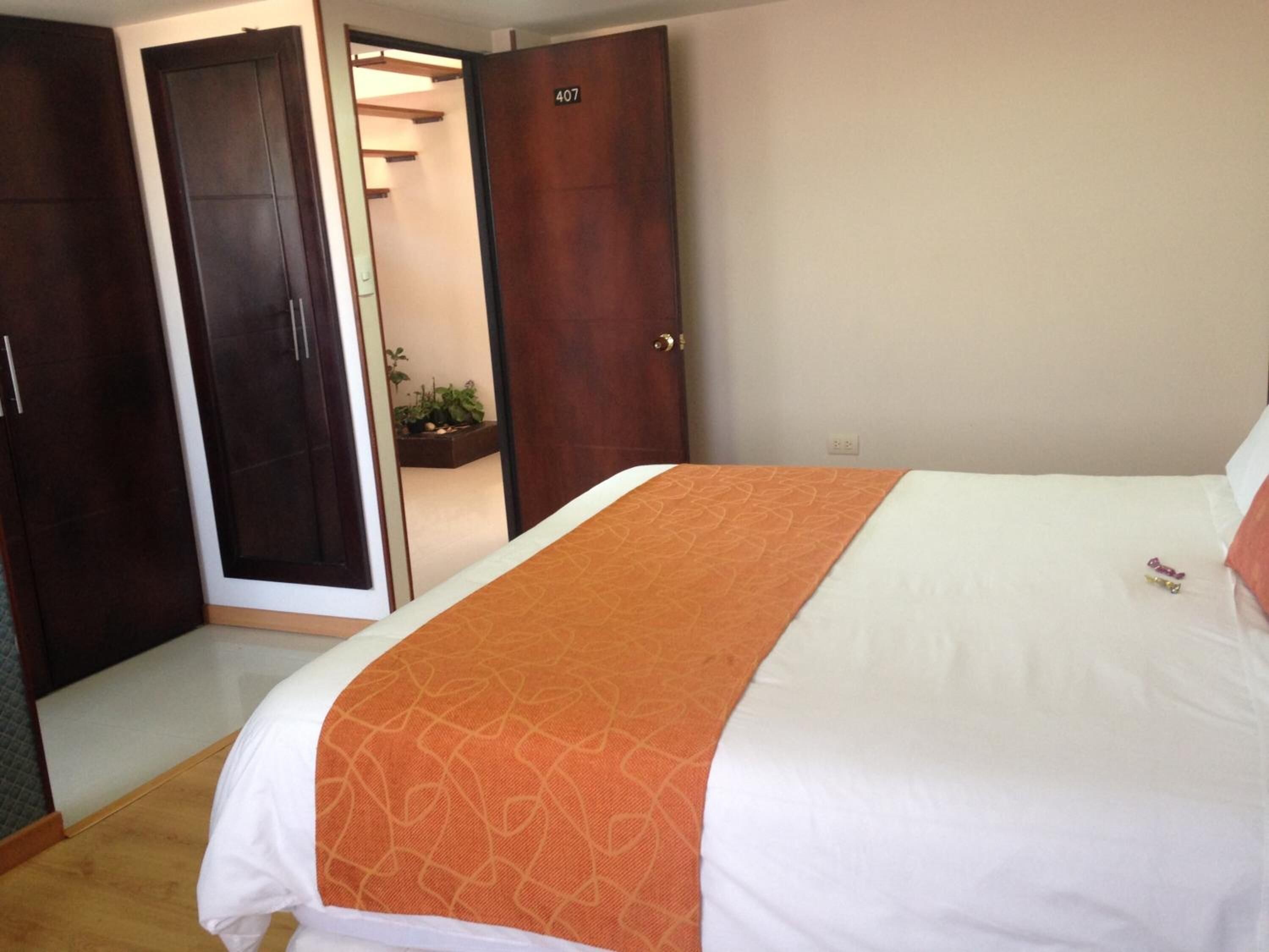 A hotel room with a bed, an orange patterned bedspread, a white pillow, and a wooden wardrobe.