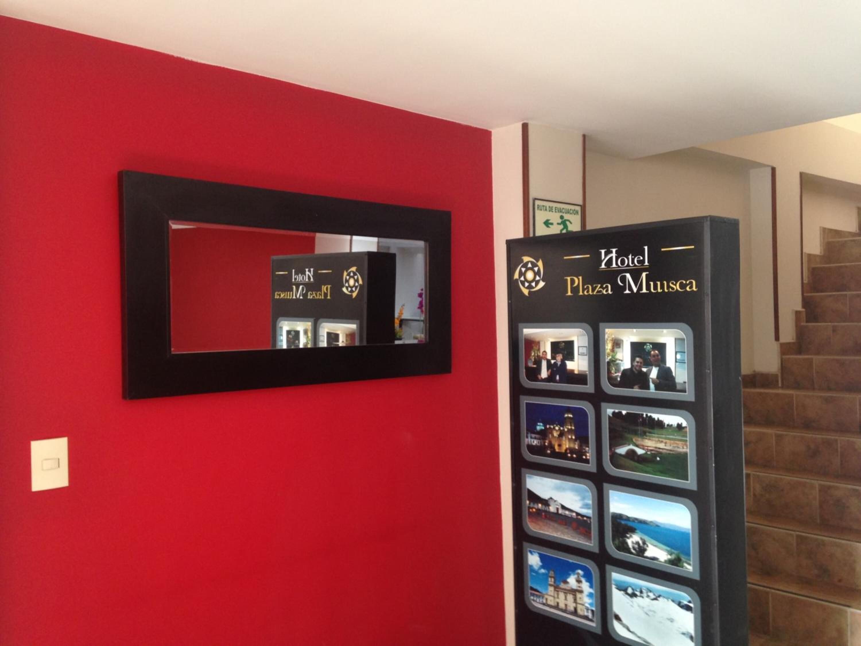 Un hall d’accueil d’hôtel avec un mur rouge, un comptoir d’accueil noir et un escalier.