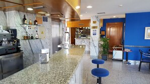 A hotel lobby with a marble reception desk, a coffee machine, and a seating area with blue stools.