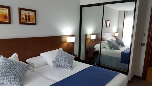 A hotel room with a large bed, two bedside tables, a nightstand, a mirror, and two wall-mounted lamps.