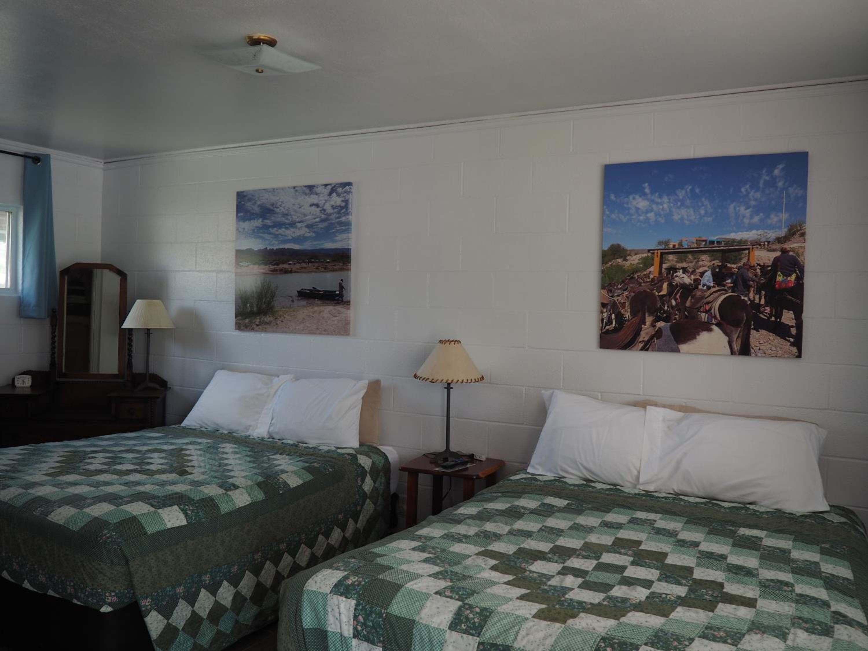 A room with two beds, a nightstand, a lamp, and two wall-mounted pictures.