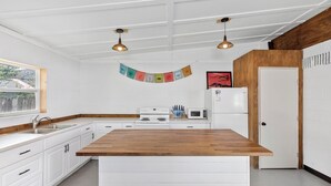 A modern kitchen with white cabinetry, a wooden island, and pendant lighting. - Desert Air Motel (Sanderson)