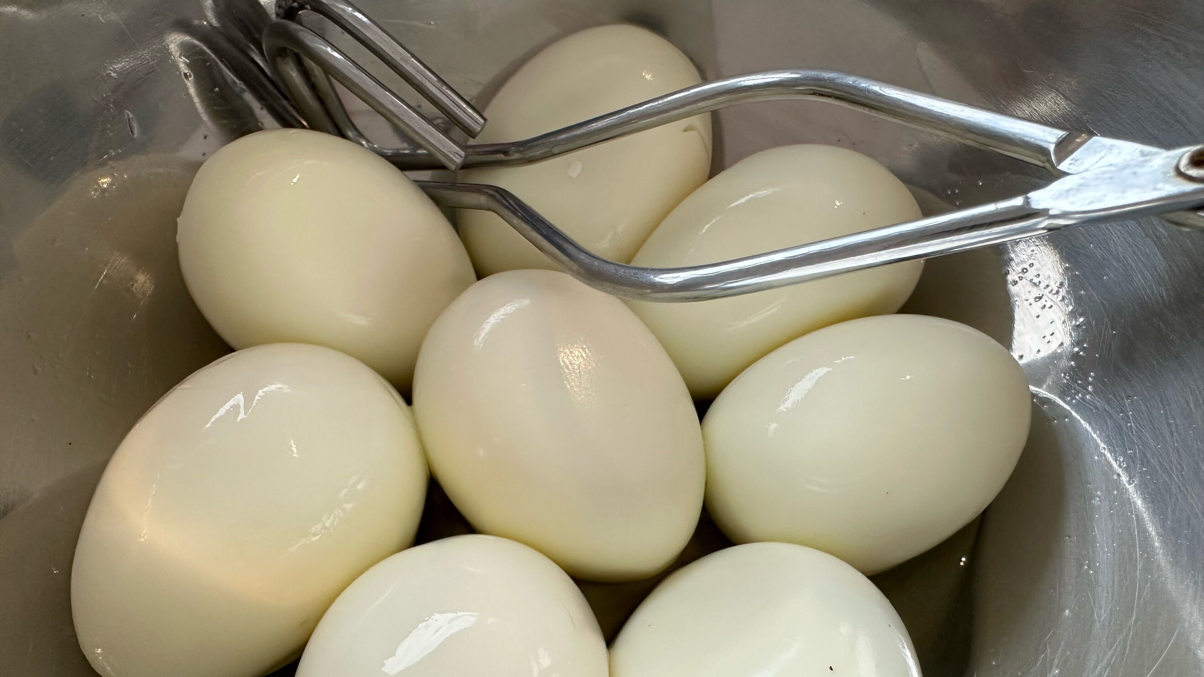 A stainless steel sink with a metal strainer holding several white eggs.