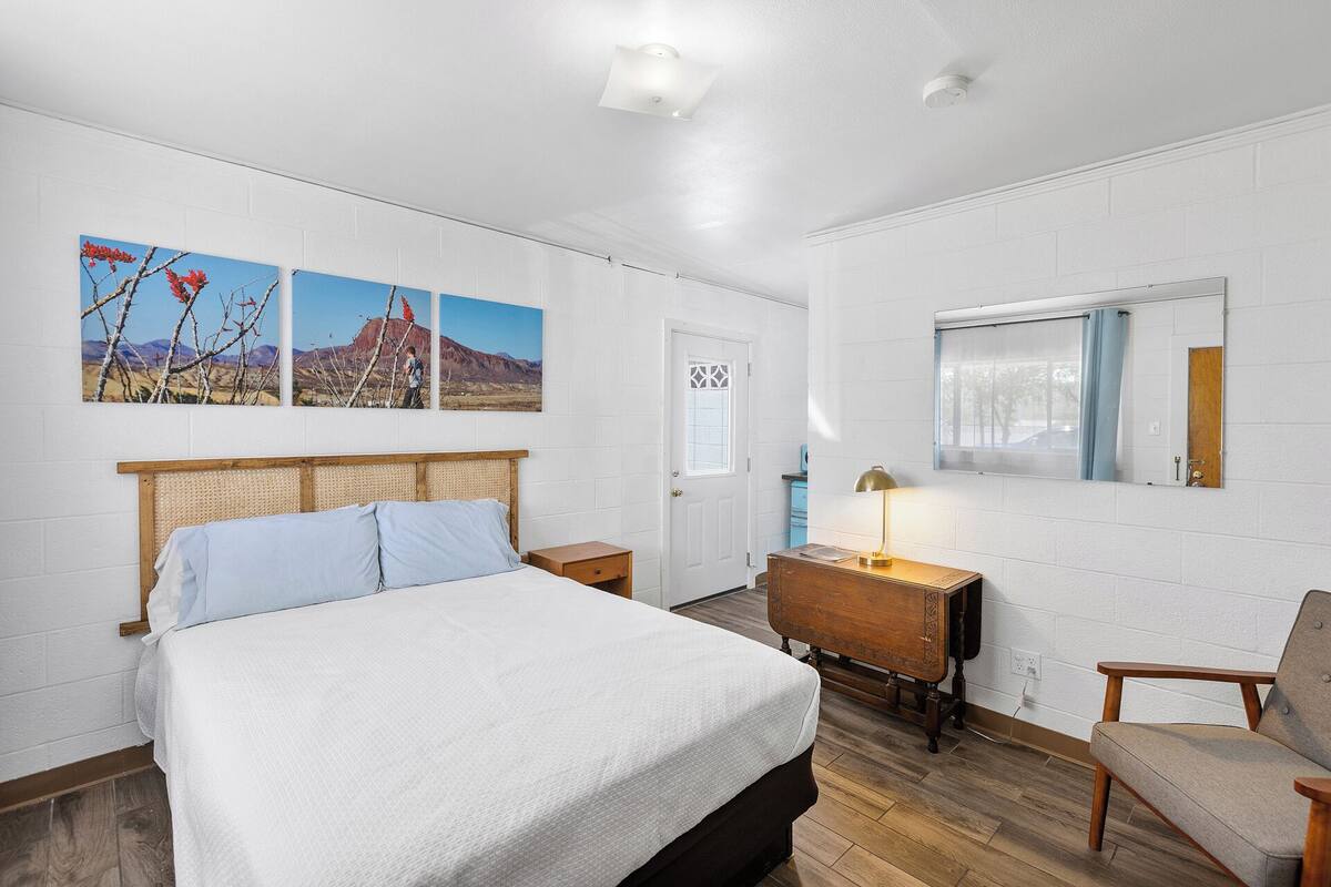 A bedroom with a large bed, a wooden dresser, a chair, and three wall-mounted paintings.