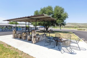 An outdoor patio with stone pillars, metal chairs, and a covered seating area. - Desert Air Motel (Sanderson)