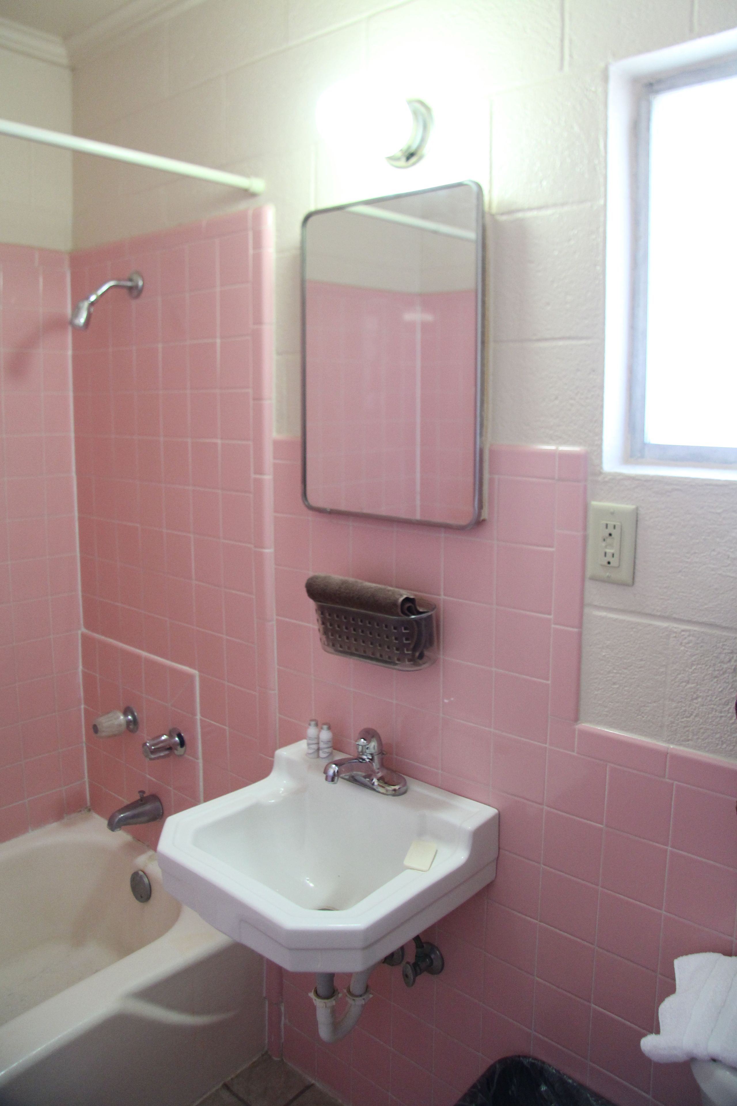 A bathroom with pink tiles, a white sink, a mirror, a shower, and a window.