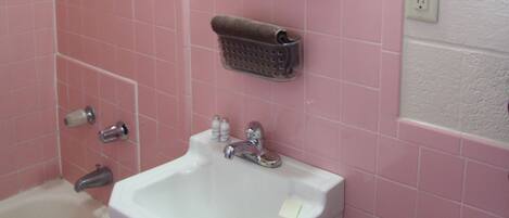 A bathroom with pink tiles, a white sink, a mirror, a shower, and a window.