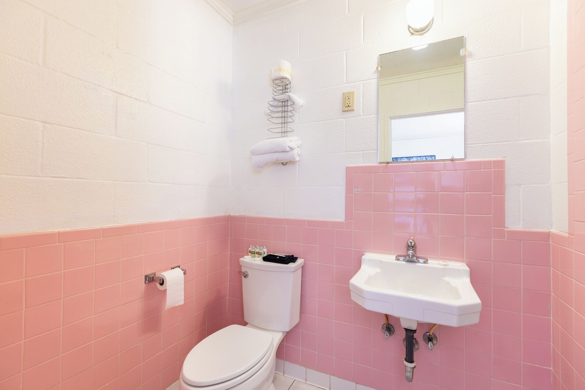 Un baño con inodoro, lavamanos y paredes de azulejos rosas.