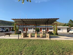 A covered outdoor seating area with stone pillars, a picnic table, and a small garden. - Desert Air Motel (Sanderson)