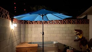 A hot tub with a blue umbrella, wooden benches, and a decorative dinosaur statue. - Desert Air Motel (Sanderson)