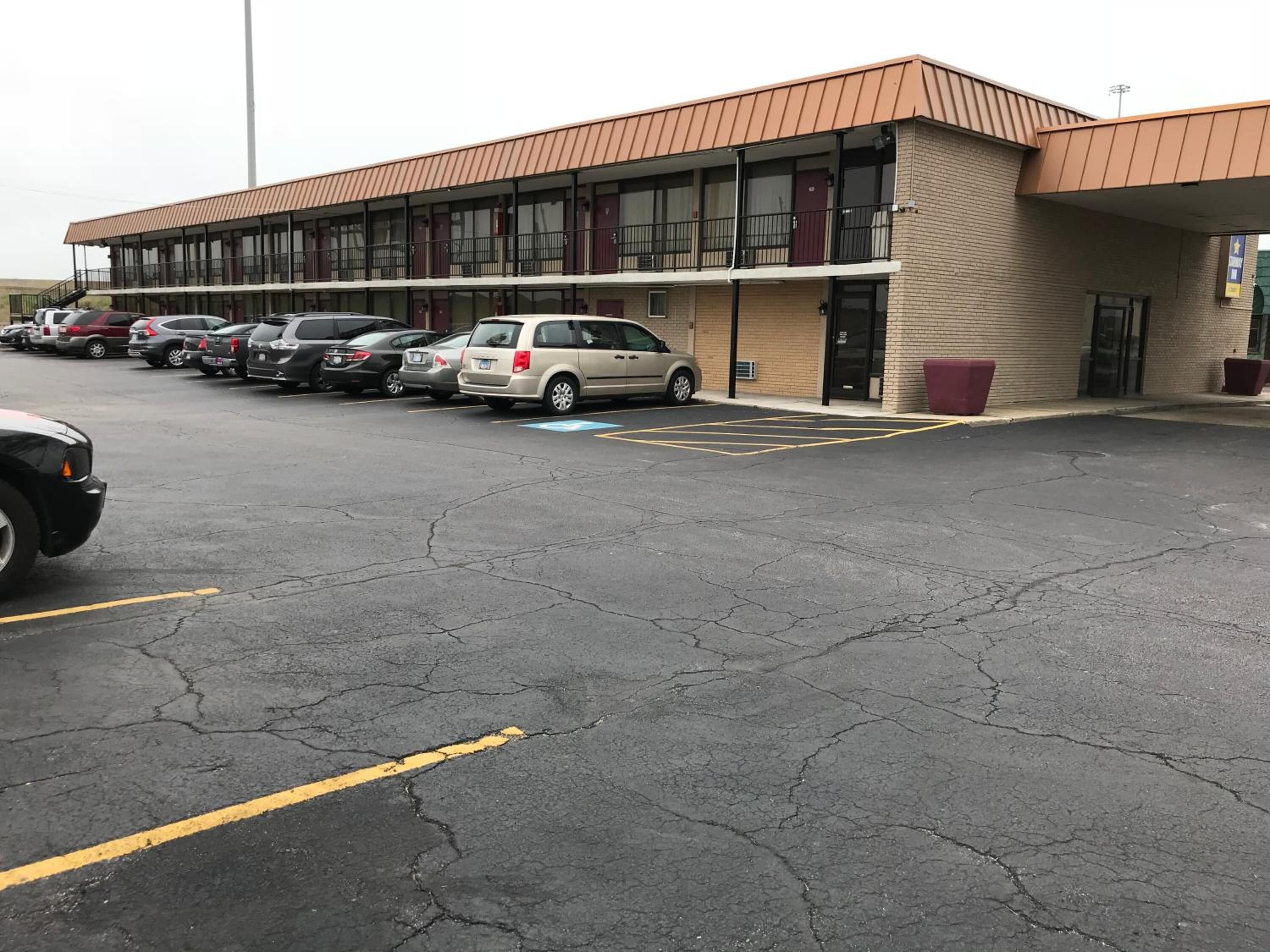 Un parking où plusieurs voitures sont garées devant un immeuble à la façade en briques et au toit plat.