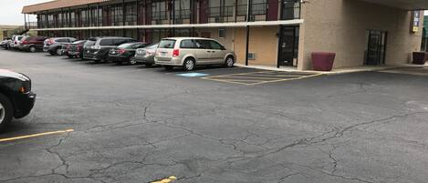 Un parking où plusieurs voitures sont garées devant un immeuble à la façade en briques et au toit plat.
