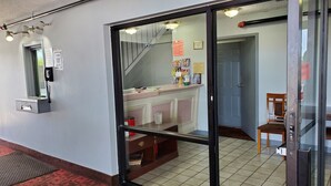 A reception area with a glass door, a desk with various items, a phone, and a chair. - Starway Inn (Lansing)