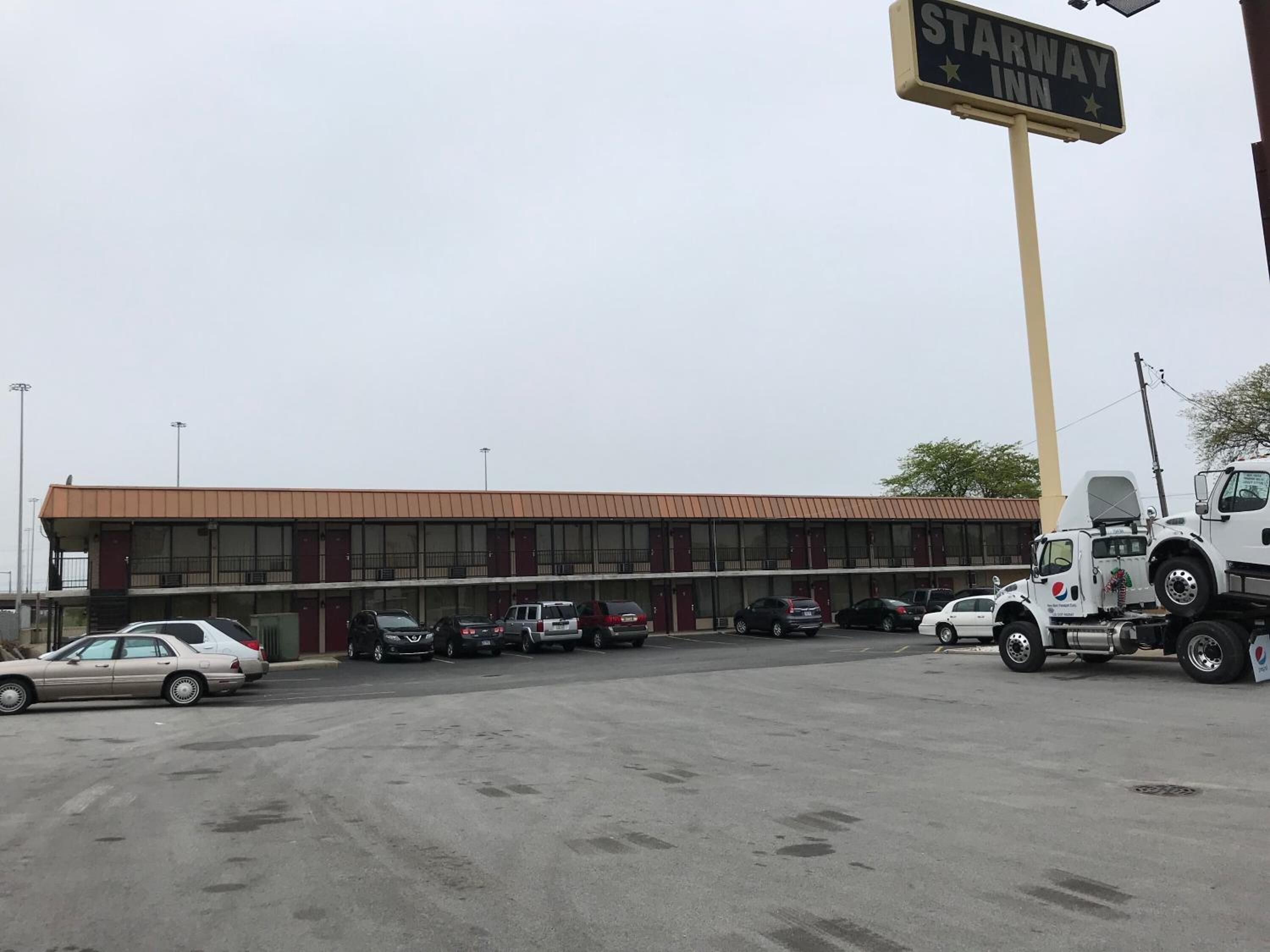 A parking lot with multiple cars and a large building with a sign reading "STARWAY INN".