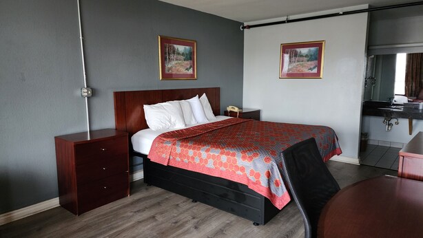A hotel room with a wooden bed, a nightstand, a desk, and a bathroom with a sink and mirror. - Starway Inn (Lansing)