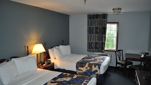 A hotel room with two beds, a desk, a chair, a lamp, and a window with curtains. - Grand Islander Hotel (Put-in-Bay)