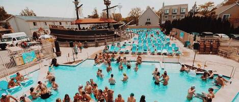 Una piscina con múltiples carriles, rodeada de sillas de descanso y un barco grande al fondo.