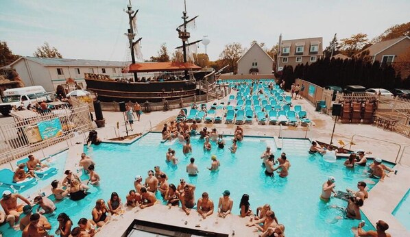 A swimming pool with multiple lanes, surrounded by lounge chairs and a large ship in the background. - Grand Islander Hotel (Put-in-Bay)