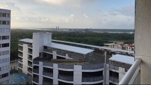 Un immeuble de grande hauteur, doté de nombreux étages, d’un espace sur le toit avec une passerelle couverte, et offrant une vue sur un paysage urbain lointain et sur la verdure.