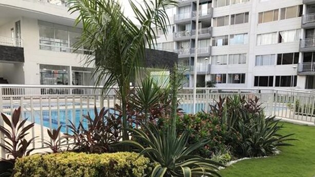 Un hôtel moderne doté d’une piscine, entouré d’un espace verdoyant bien entretenu et d’une clôture blanche.
