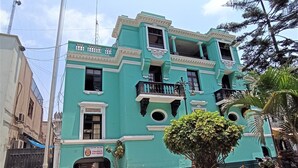 A teal building with a flagpole, a gated entrance, and a small garden with flowers.