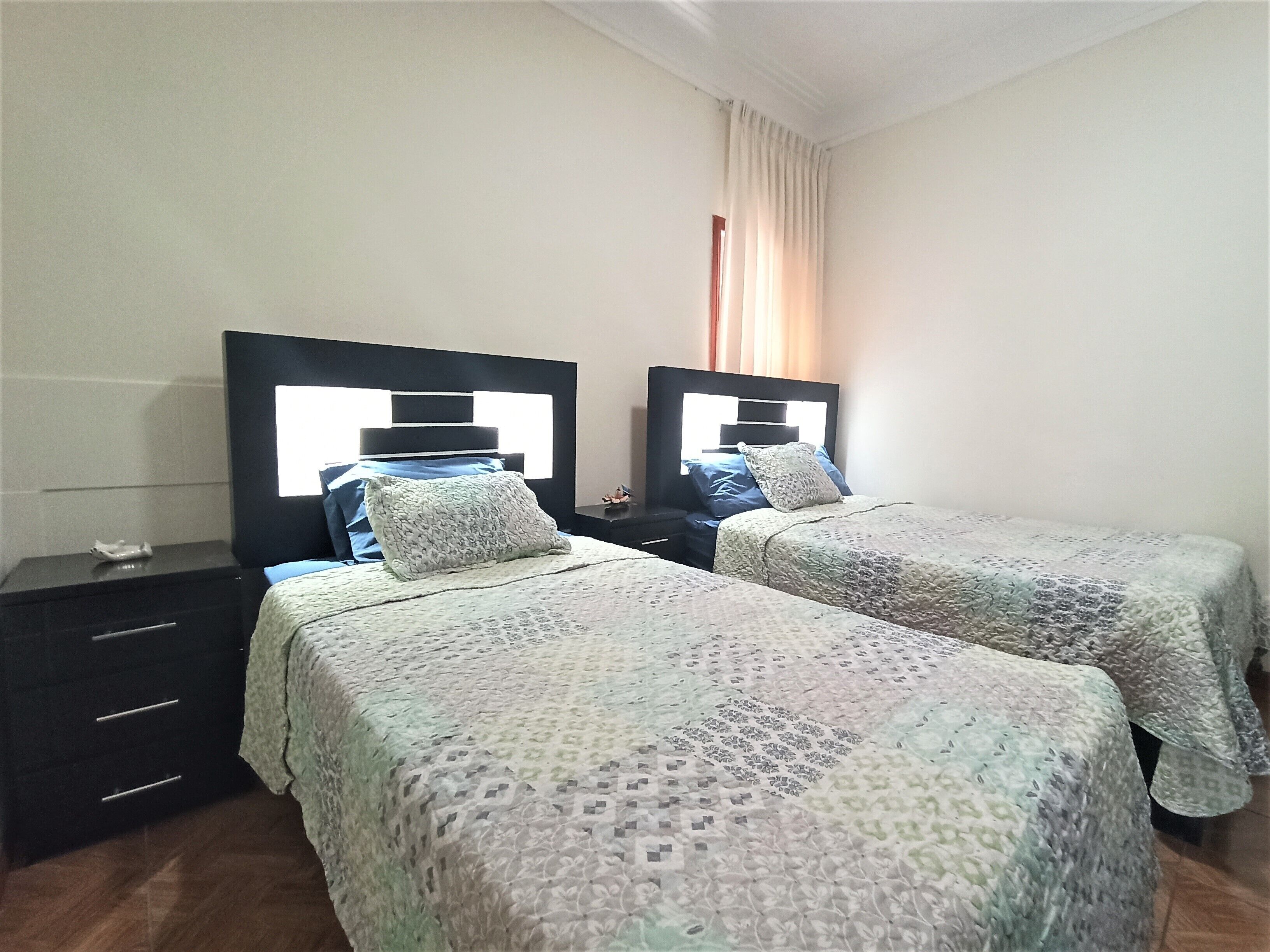 A hotel room with two beds, each with a headboard and a bedside table.