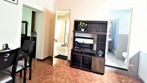 A living room with a TV, a wooden floor, a black entertainment unit, and a dining area with chairs.