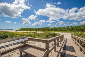 A wooden boardwalk leading to a beach with a clear sky and clouds. - Beachfront 2BR/2BA condo with pool, WiFi, and heated pool access. (Marco Island)