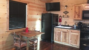 Interior de una cabaña de madera con una mesa de comedor, sillas, un refrigerador, un lavaplatos y una estufa.