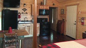 Interior de una cabaña de madera con cocina, comedor y una puerta que da a otra habitación.